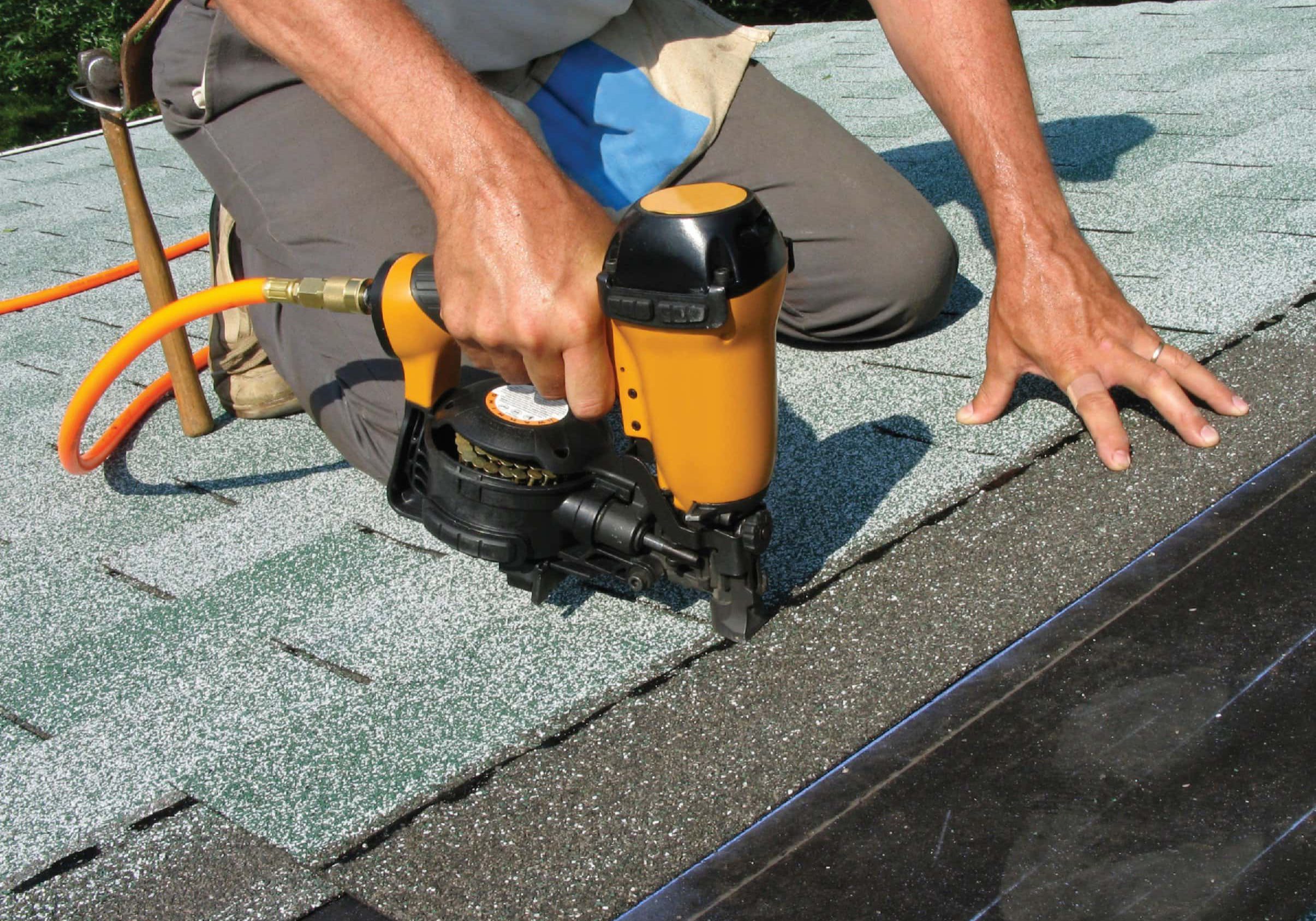 Person using nail gun on roof shingles.